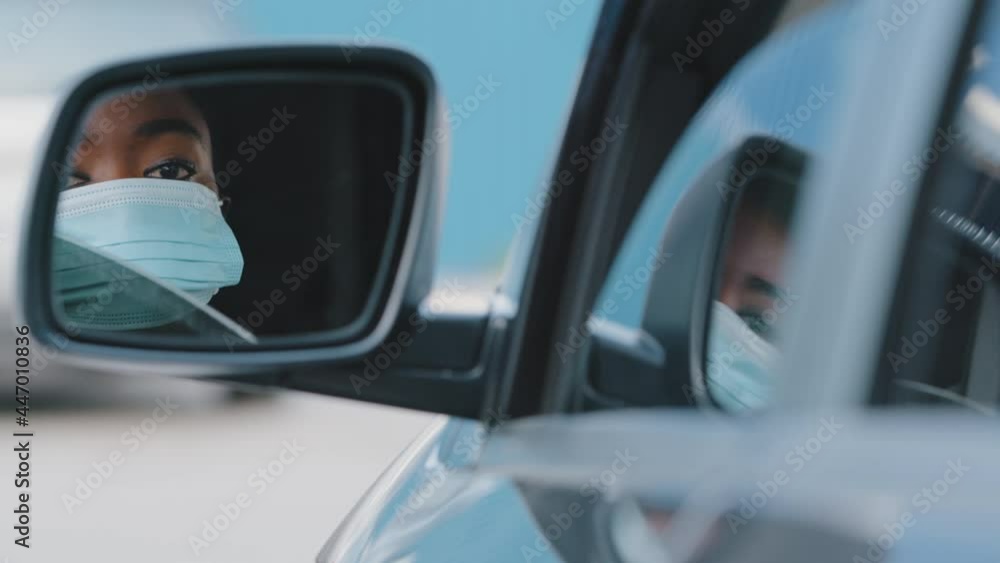 Close-up reflection in mirror african american young beautiful girl afro woman driver wears medical protective face mask lowers glass window in car sits in auto feels lack of fresh air in automobile Close-up reflection in mirror african american young beautiful girl afro woman driver wears medical protective face mask lowers glass window in car sits in auto feels lack of fresh air in automobile