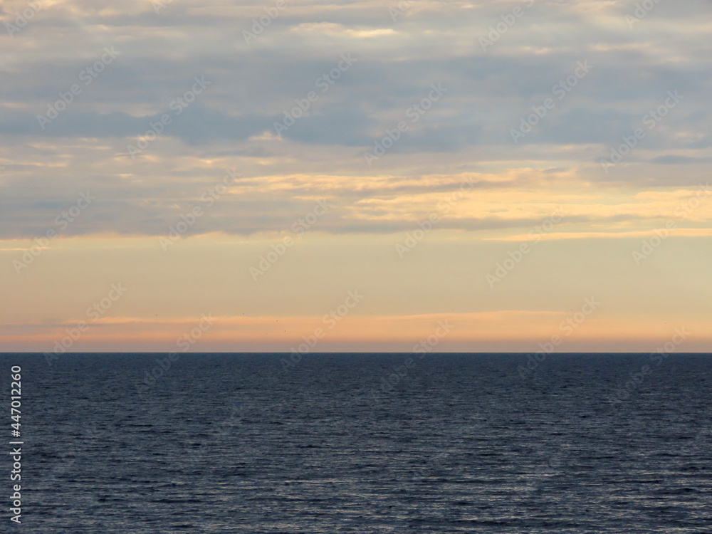 Pastel colour clouds shortly before sunset over calm sea. Background with yellow, blue, orange, beige colors