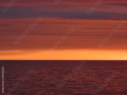 Dramatic dark clouds at sunset over calm sea. Background with black, red, orange, yellow colors