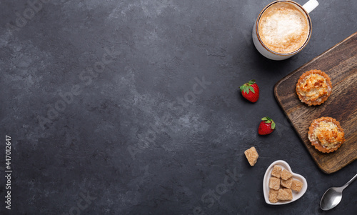 Ceramic mug with coffee, tasty cakes and strawberries on dark stone background. Top view. Copy space