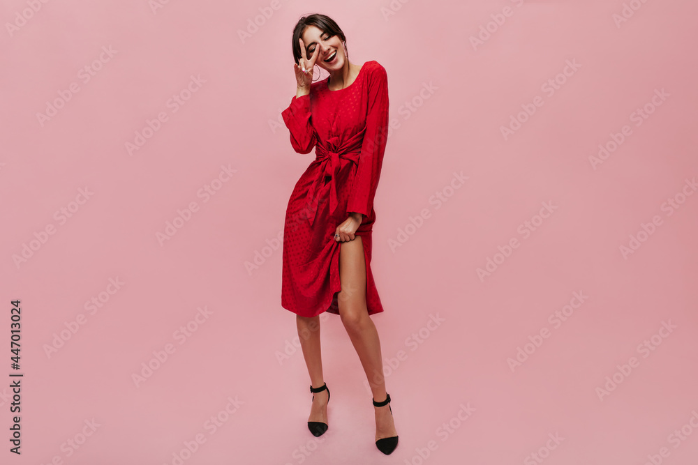 Full length photo of fashionable cool lady with round big earrings in midi red dress and black heels showing peace sign and smiling.