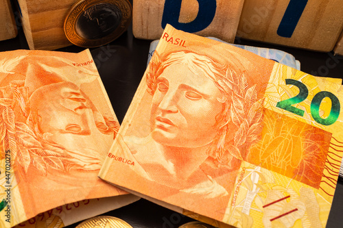 Real - BRL, dinheiro do Brasil. Duas cédulas de vinte reais do Real brasileiro sobre uma mesa escura com alguns cubos de madeira e moedas na composição.
 photo