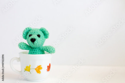 a small knitted bear sits in a mug. teddy bear knitted from threads
