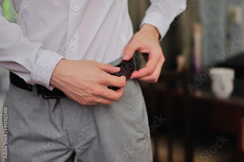 a man fastens a belt on his trousers with a white shirt.