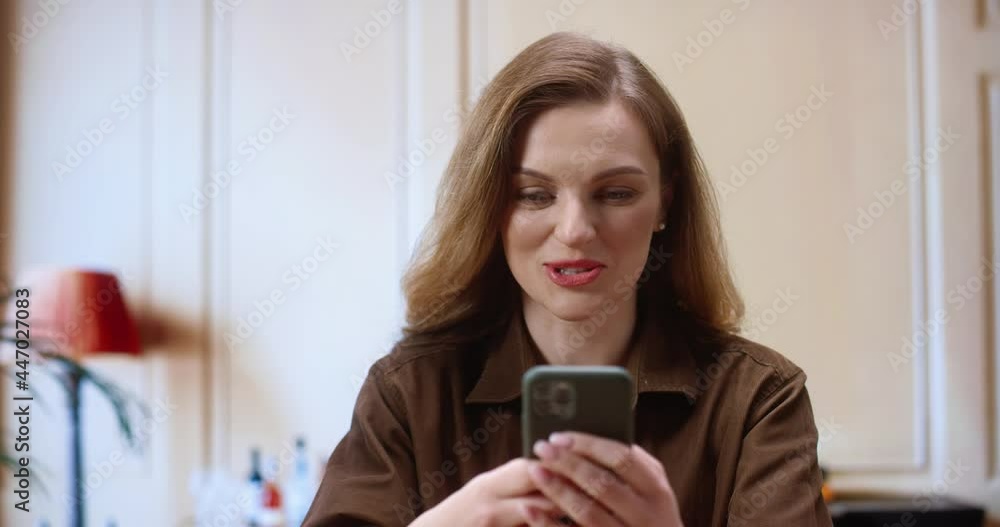 Wow. Smiling surprised woman holding her smartphone and rejoicing while sitting at the office. Portrait of a positive girl sitting indoors and typing at the phone while feeling pleasure emotions Wow. Smiling surprised woman holding her smartphone and rejoicing while sitting at the office. Portrait of a positive girl sitting indoors and typing at the phone while feeling pleasure emotions