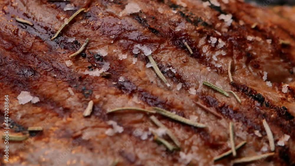 Roasting juicy meat steak on a grill plate sprinkled with salt flakes and herbs. Healthy food concept. Roasting juicy meat steak on a grill plate sprinkled with salt flakes and herbs. Healthy food concept.
