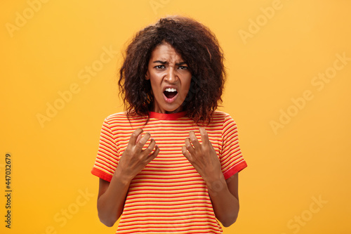 Waist-up shot of woman feeling upset feeling unfair things happened complaining and whining with regret frowning gesturing with palms near breast standing over orange background photo