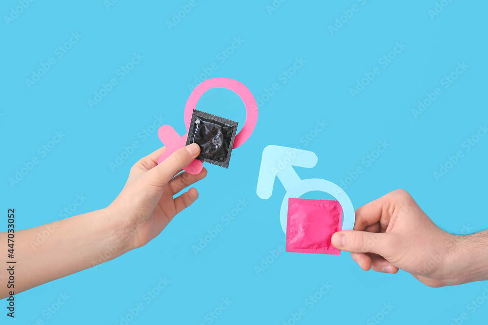 Hands with condoms and symbols of woman and man on color background Hands with condoms and symbols of woman and man on color background