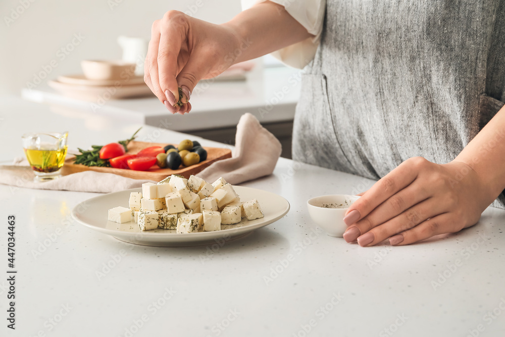 Woman adding spices to delicious feta cheese on table