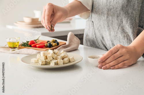 Woman adding spices to delicious feta cheese on table