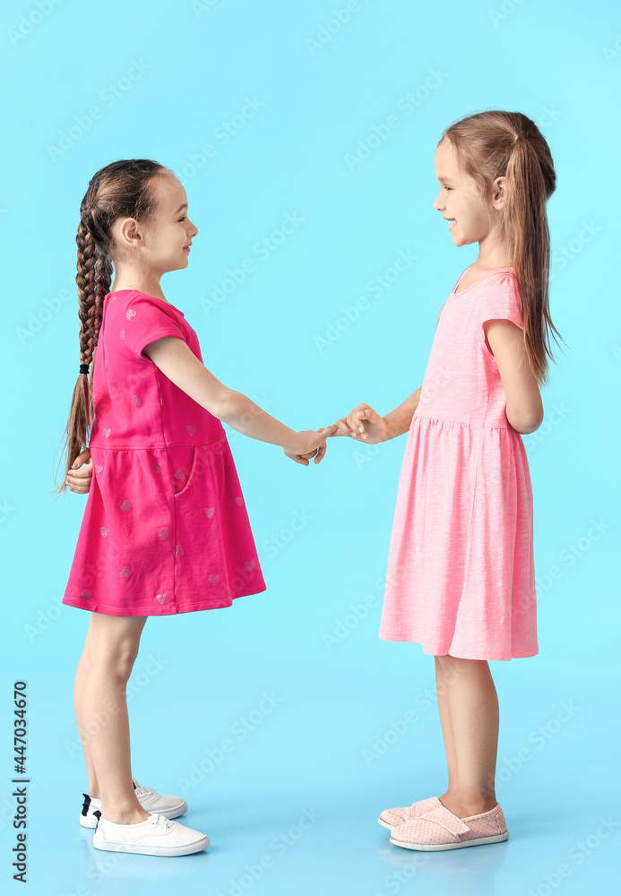 Cute little sisters making pinky promise on color background Cute little sisters making pinky promise on color background