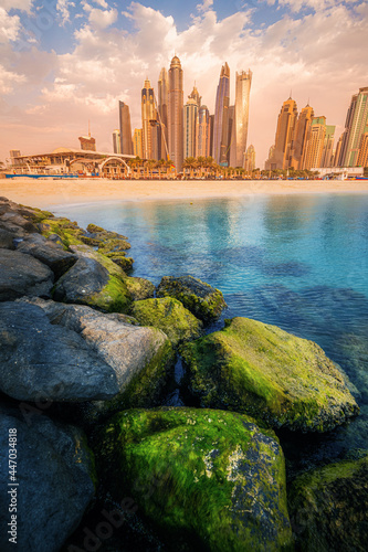 Majestic rocks breakwaters in the foreground with the azure waters of the Persian Gulf and colorful skyscrapers in the Marina and JBR bay area in Dubai