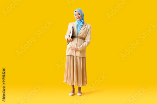 Pregnant Muslim woman with clipboard on color background