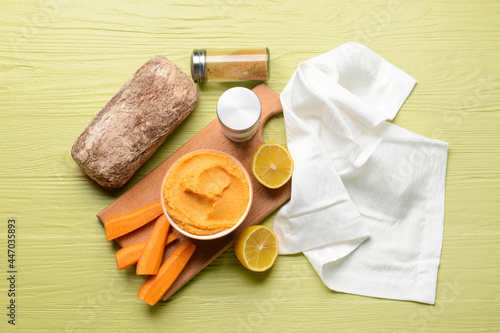 Bowl with tasty carrot hummus, lemon and bread on color wooden background