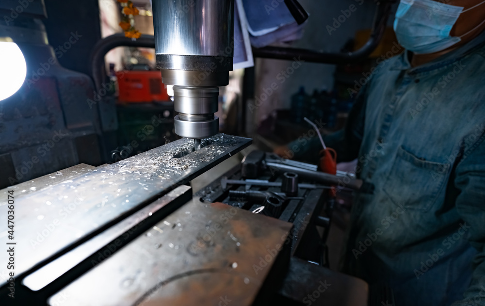 A man wear surgical mask working with milling machine. Tool for cut metal workpiece. Vertical milling machine with cemented carbide milling cutter. Steel manufacturing industry. Milling process. A man wear surgical mask working with milling machine. Tool for cut metal workpiece. Vertical milling machine with cemented carbide milling cutter. Steel manufacturing industry. Milling process.