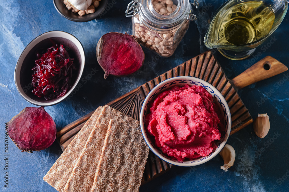 Bowl with tasty beet hummus and crackers on color background