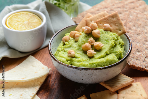 Bowl with tasty green pea hummus, chickpeas and crackers on table, closeup