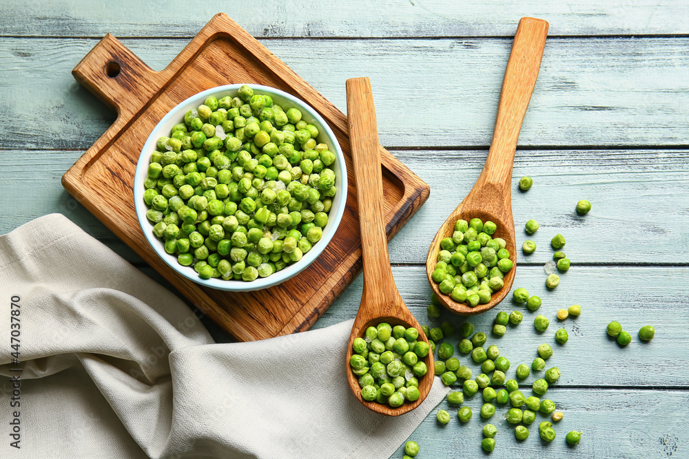 Spoons and bowl with frozen green peas on color wooden background Spoons and bowl with frozen green peas on color wooden background
