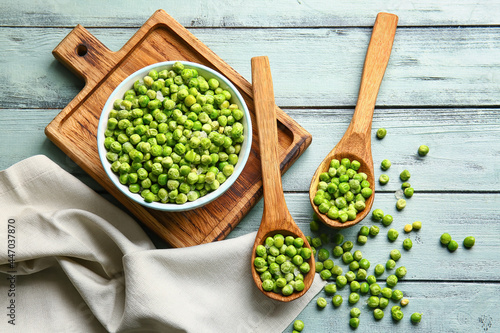 Spoons and bowl with frozen green peas on color wooden background
