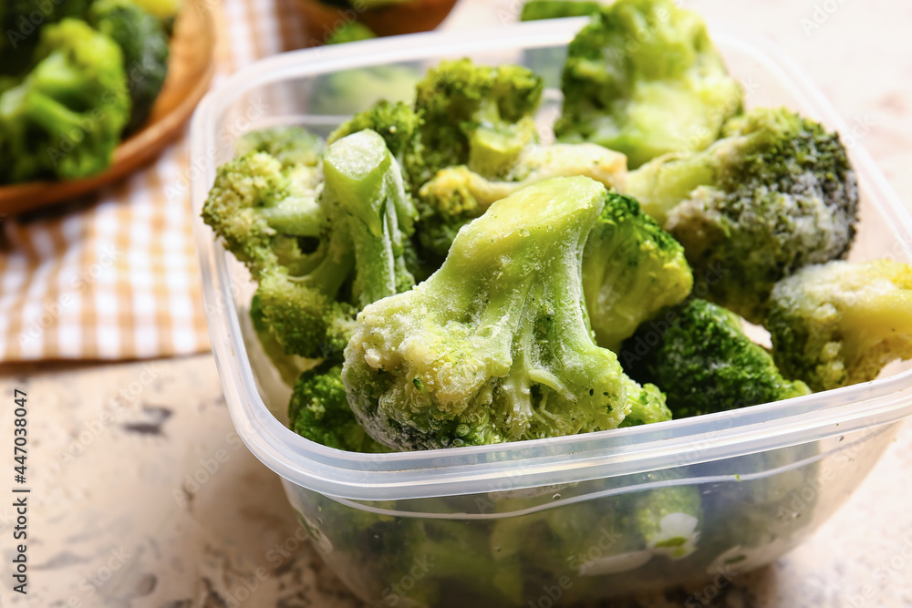 Container with frozen broccoli on light background