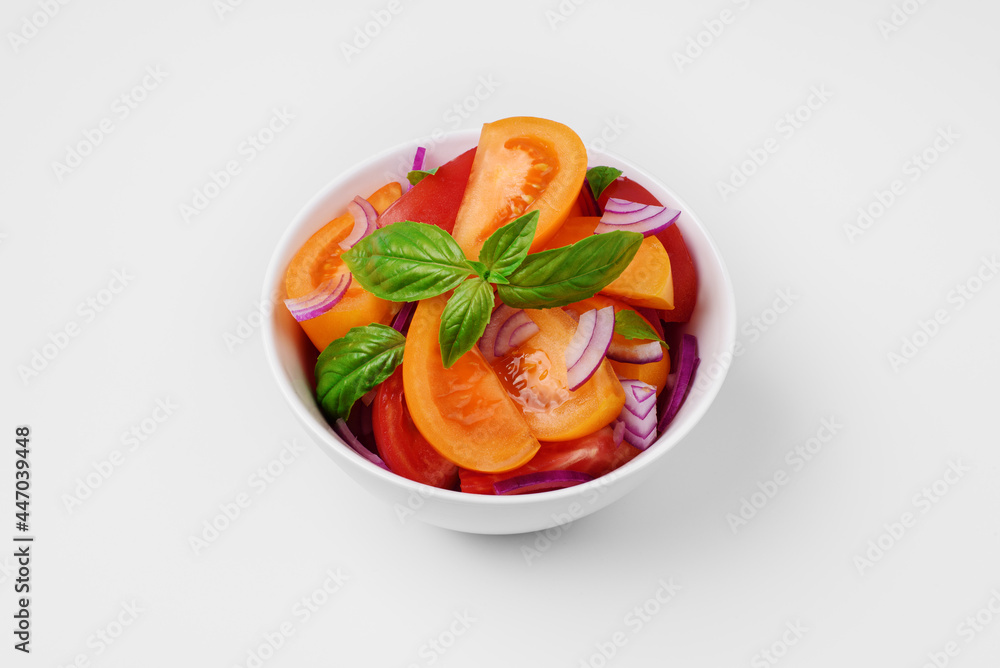 Bright summer salad of red and yellow tomatoes, spanish red onions and basil on white background. Fresh colorful tomato salad with farm organic vegetables. Clean food concept.