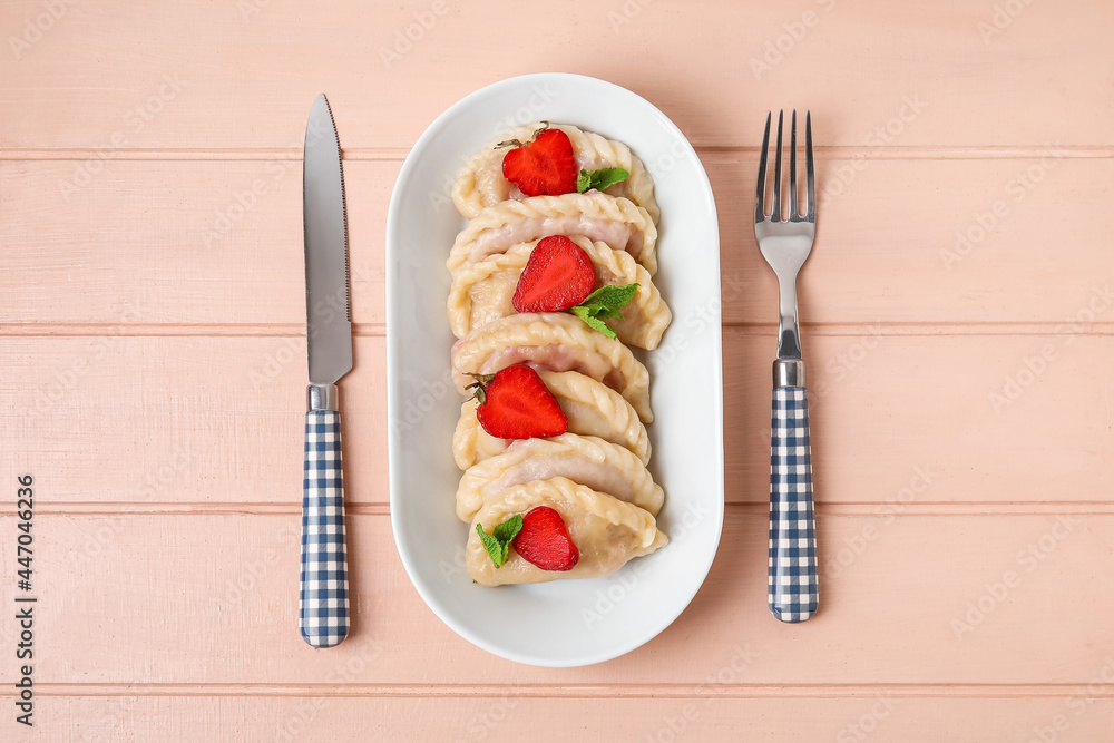 Plate with tasty strawberry dumplings on color wooden background