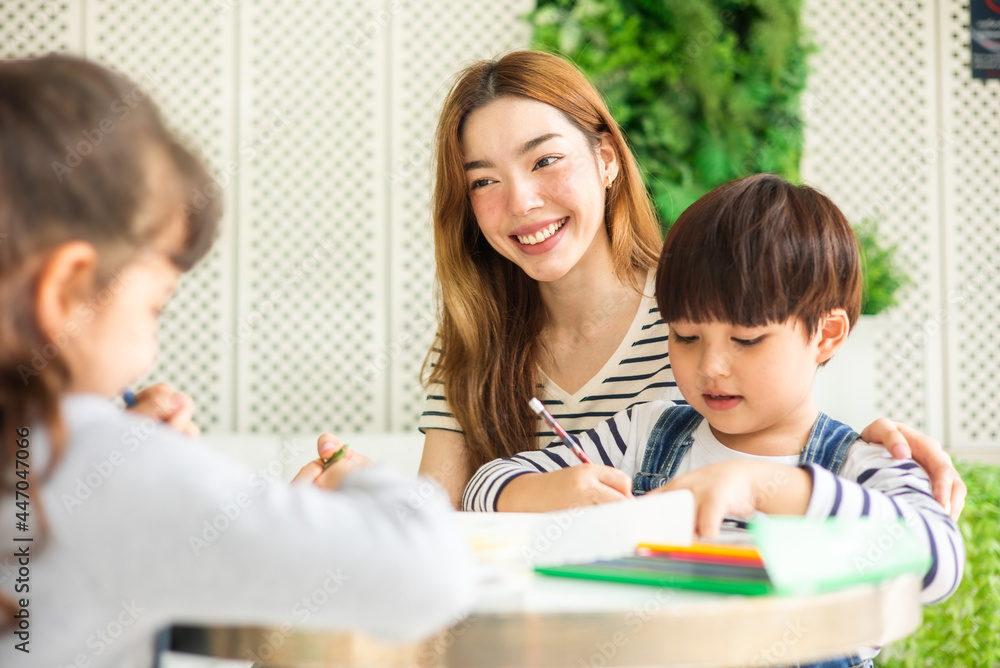 happy loving family. pretty young mother reading a book and drawing to her daughter and son.Mother teach Asian preschool student do homework by reawing by a color. happy loving family. pretty young mother reading a book and drawing to her daughter and son.Mother teach Asian preschool student do homework by reawing by a color.
