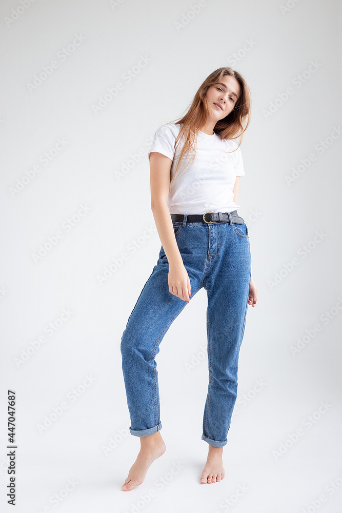 young attractive caucasian woman with long hair in t-shirt and blue jeans isolated on white studio background. skinny pretty female posing on cyclorama with bare feet. model tests of beautiful lady young attractive caucasian woman with long hair in t-shirt and blue jeans isolated on white studio background. skinny pretty female posing on cyclorama with bare feet. model tests of beautiful lady