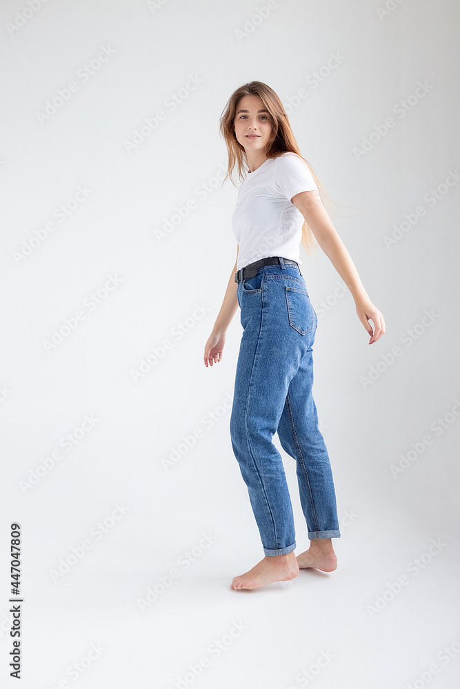 young attractive caucasian woman with long hair in t-shirt and blue jeans isolated on white studio background. skinny pretty female posing on cyclorama with bare feet. model tests of beautiful lady young attractive caucasian woman with long hair in t-shirt and blue jeans isolated on white studio background. skinny pretty female posing on cyclorama with bare feet. model tests of beautiful lady