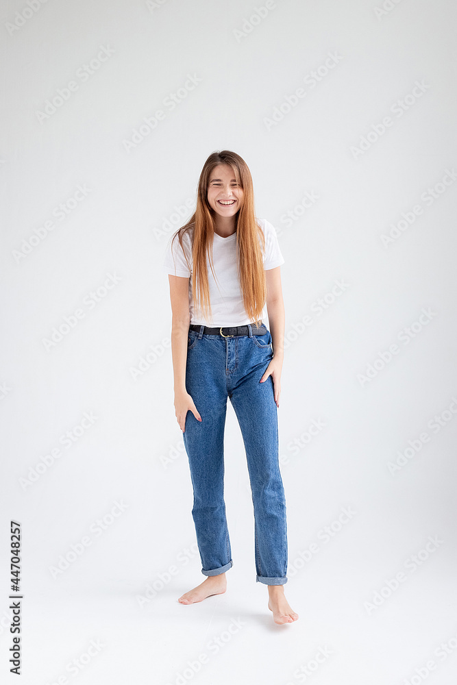 young attractive caucasian woman with long hair in t-shirt and blue jeans isolated on white studio background. skinny pretty female posing with bare feet. beautiful lady laughing on cyclorama young attractive caucasian woman with long hair in t-shirt and blue jeans isolated on white studio background. skinny pretty female posing with bare feet. beautiful lady laughing on cyclorama