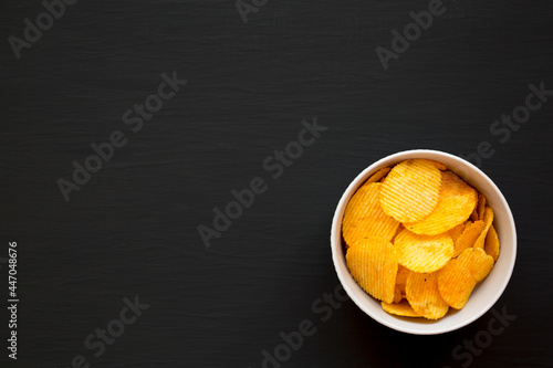 Ruffled Cheese Potato Chips in a Bowl on a black background, top view. Flat lay, overhead, from above. Copy space.
