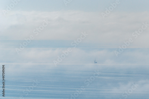 Sailboat sailing in the high seas covered in clouds and fog.