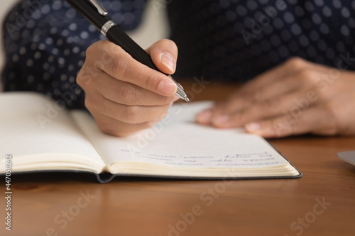 Close up young woman taking notes in notebook, holding pen, successful businesswoman entrepreneur planning workday in organizer, meetings, managing time, student preparing to exam, handwriting