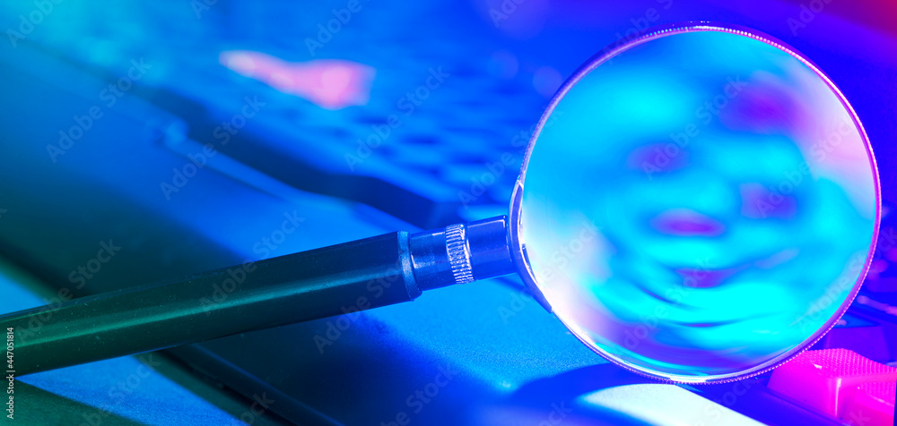 Magnifying glass on laptop keyboard in neon light Magnifying glass on laptop keyboard in neon light