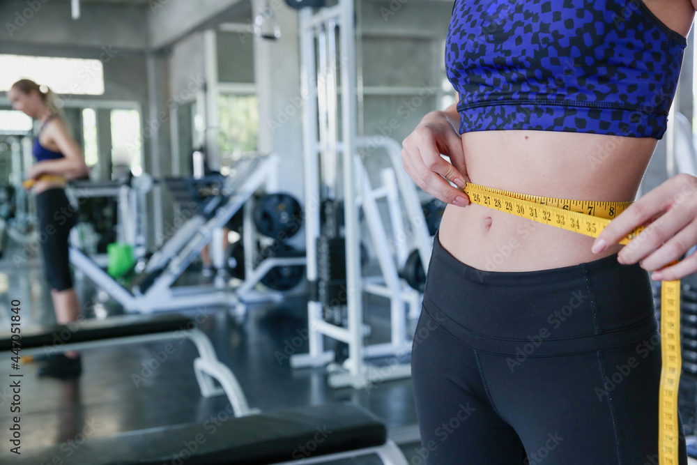 Slim woman measuring her waist at gym. Slim body woman measuring her waist at gym. Slim woman measuring her waist at gym. Slim body woman measuring her waist at gym.