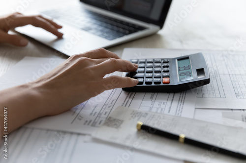 Crop close up of woman manage household budget count on machine make payment on computer. Female calculate expenses expenditures pay bills taxes online on laptop. Finance, banking concept.