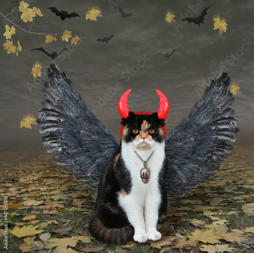 A colored cat with bird wings and red devil horns is in the fall forest for Halloween.