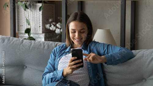 Lovely young woman spend time use smartphone, sit on sofa in living room hold cellphone enjoy chat in social media, search buy goods fashion clothes via e-commerce retail services application concept