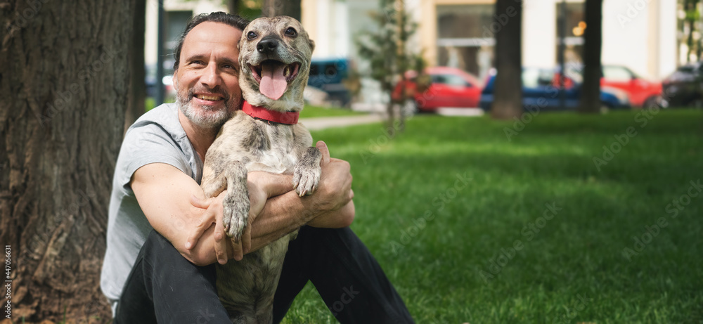 Happy attractive mature man 50 years old resting on the grass while walking with his dog in his arms