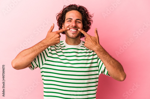 Young caucasian man isolated on pink bakcground smiles, pointing fingers at mouth.
