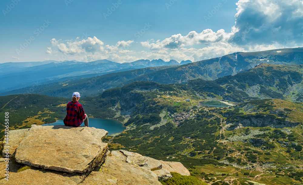 A young girl enjoys a beautiful view sitting on the rock from the top. Travel in the mountains.