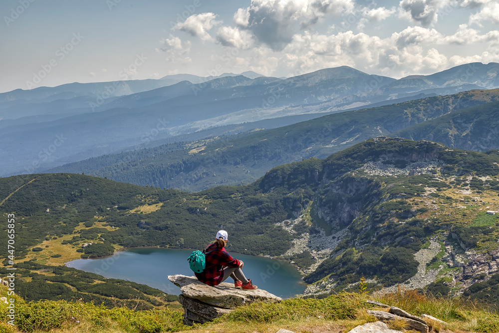 Fototapeta premium A young girl enjoys a beautiful view sitting on the rock from the top. Travel in the mountains.