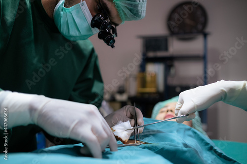 Group of professional doctor wearing uniform and face mask doing surgery in the hospital in the operating room under light. Doctor using scisor and forceps to help patient. Medical health and cure photo