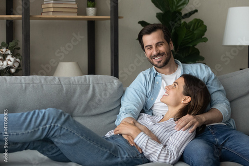 Young couple relax on comfy sofa in living room, carefree wife lean back on beloved husband enjoy conversation feeling love satisfaction reposing at modern home. Date, homeowner family, tenant concept