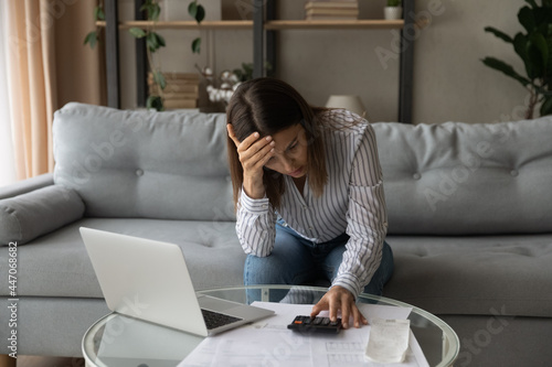 Desperate young woman sit on sofa at home calculates expenses feeling stressed about bank loan payments, lack of money, financial problems, thinking of unpaid taxes, bankruptcy, overdue bills concept