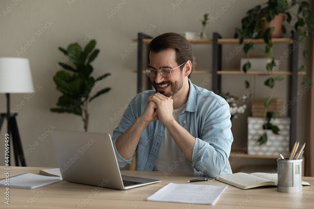 Man in glasses sit at desk in office smile looks at laptop screen, take  break distracted
