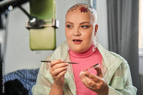 Blogger with colored patterns at her head preparing makeup in front of smartphone photo