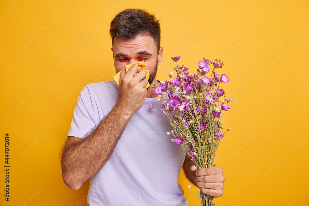 © WHstudio Leushin N - Seasoanl allergies and health concept. Unhappy man has runny nose and red swollen eyes uses handkerchief feels allergic to wild flowers poses against yellow background. Reaction on allergen. © WHstudio Leushin N - Seasoanl allergies and health concept. Unhappy man has runny nose and red swollen eyes uses handkerchief feels allergic to wild flowers poses against yellow background. Reaction on allergen.