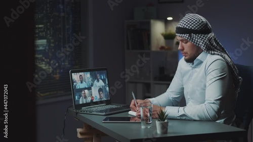 Arabic government official with kandora participating in online international medical conference. He making notes and listening to the discussion.