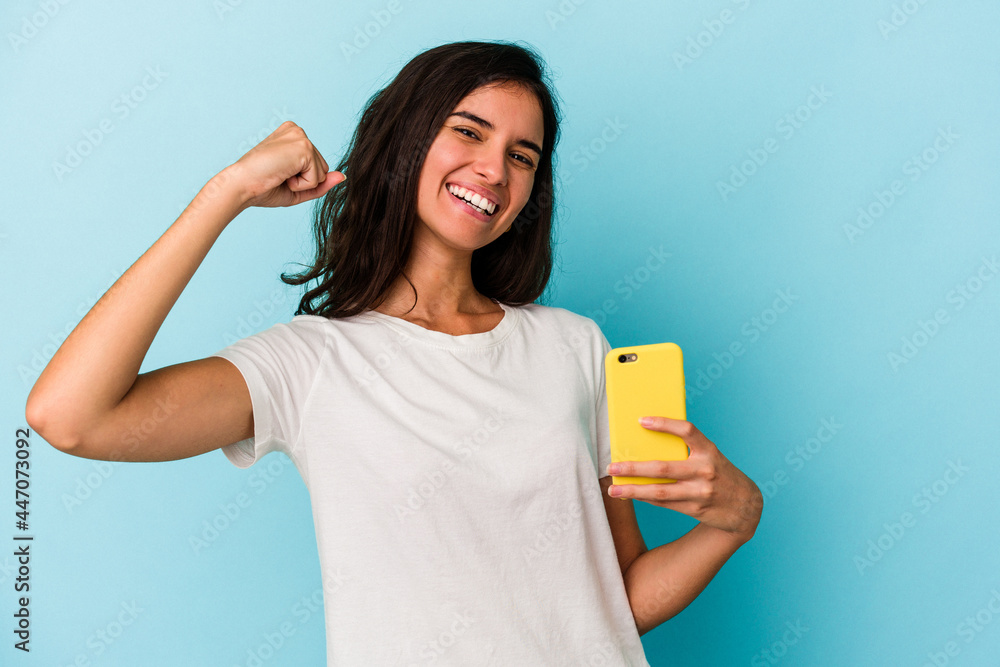 Young caucasian woman holding a mobile phone isolated on blue background raising fist after a victory, winner concept.